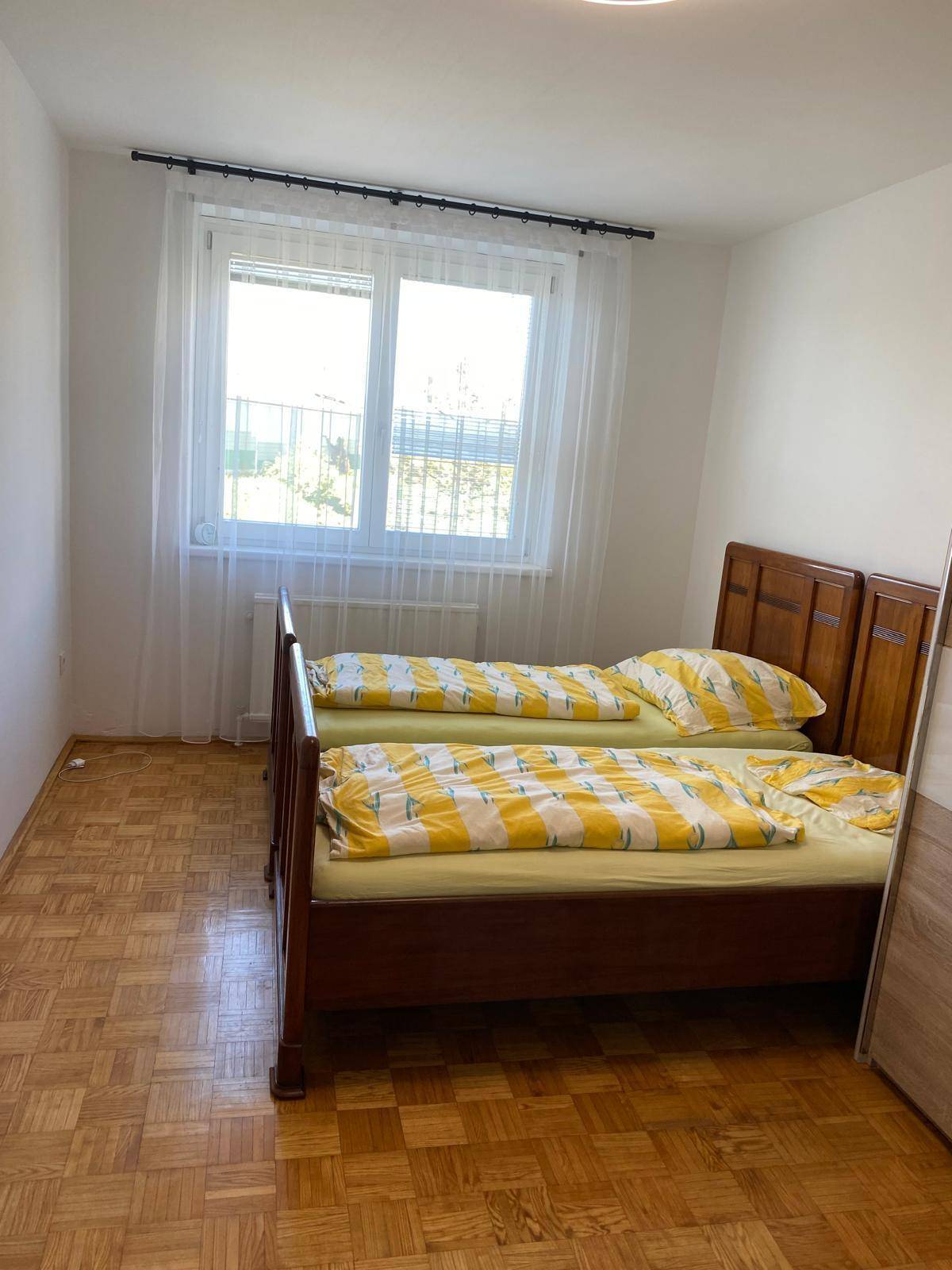 Helles Schlafzimmer mit zwei Einzelbetten, Parkettboden und großem Fenster.