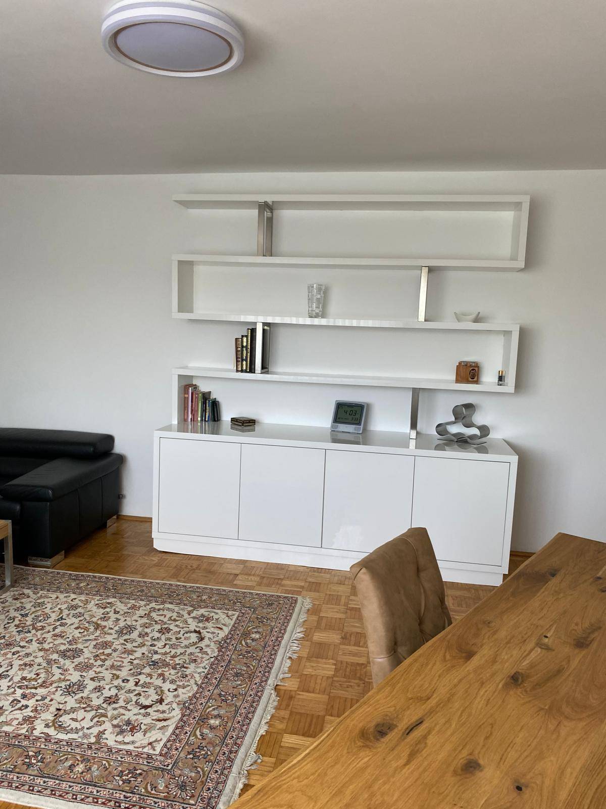 Heller Wohnbereich mit modernem weißen Sideboard, Regalen und Holzesstisch.