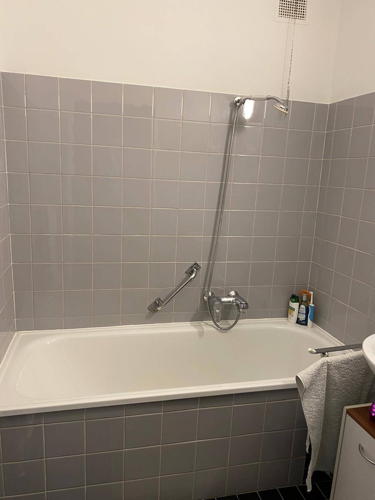 Badezimmer mit Badewanne und grauen Fliesen an den Wänden.