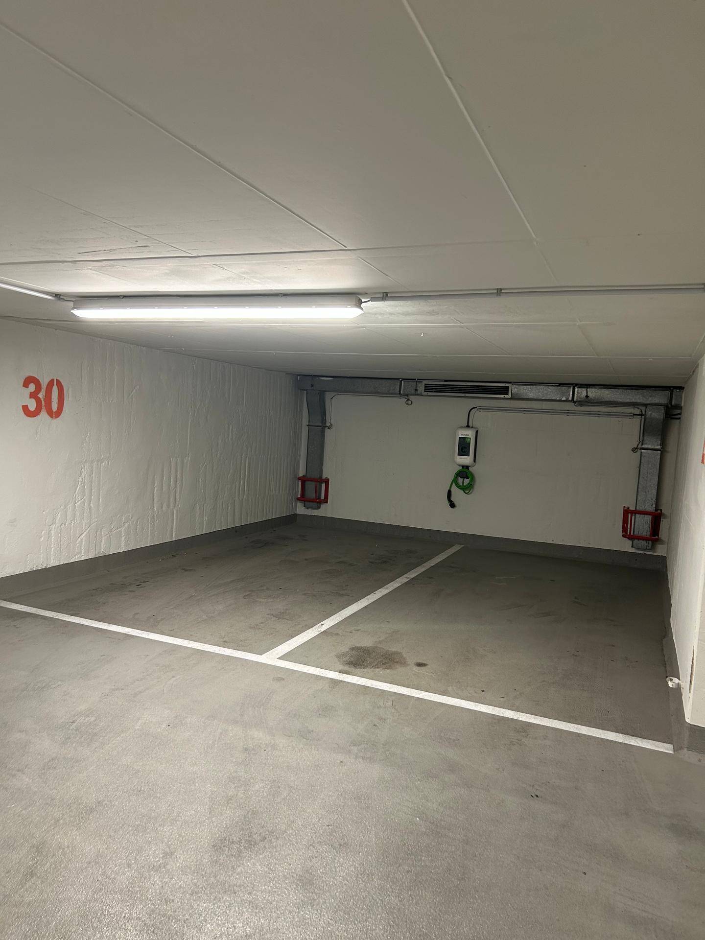 Heller Tiefgaragenstellplatz mit moderner Ladestation für Elektroautos und nummerierter Kennzeichnung.