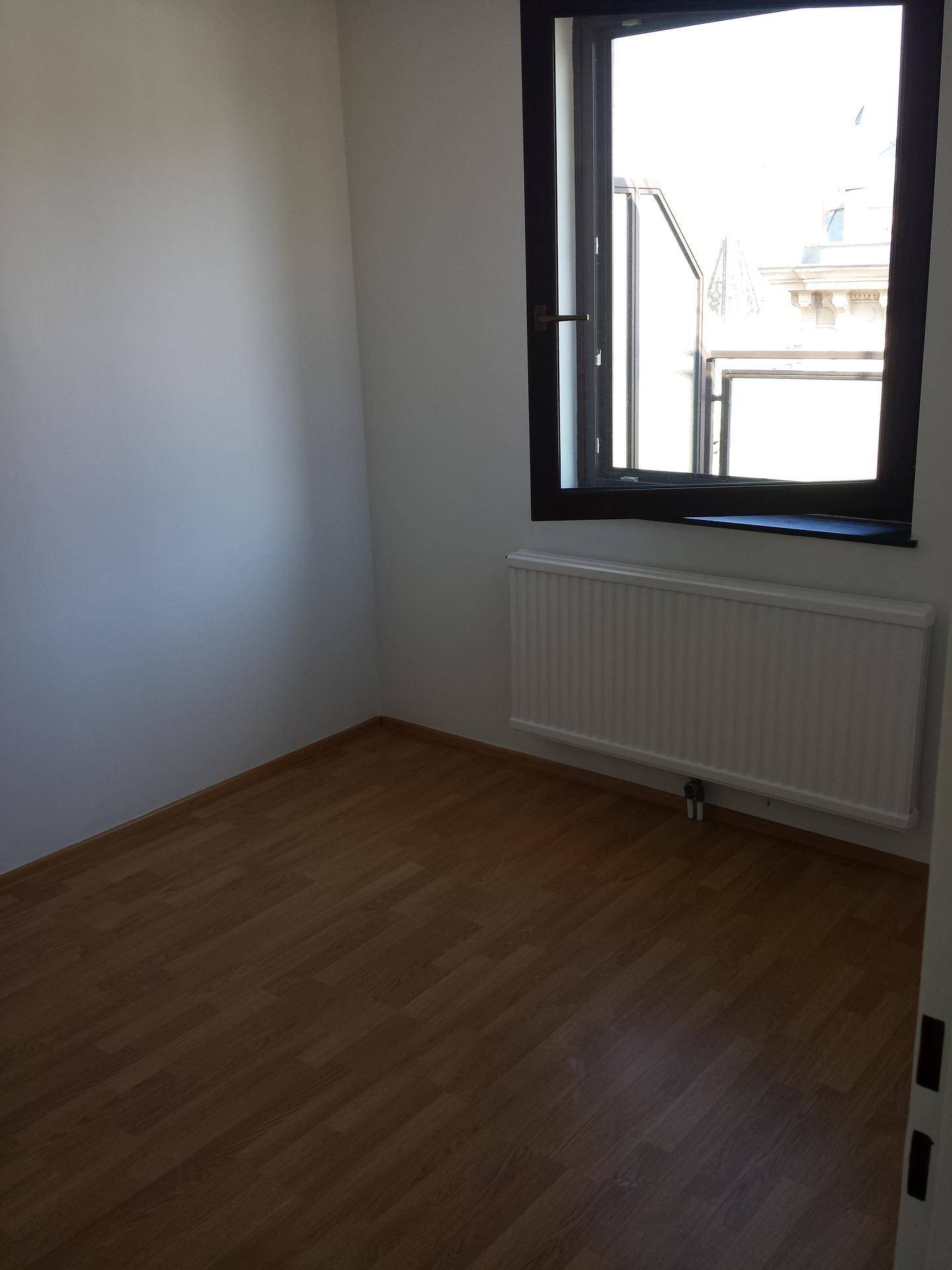 Leerer Raum mit Laminatboden, einem Fenster und Heizkörper.