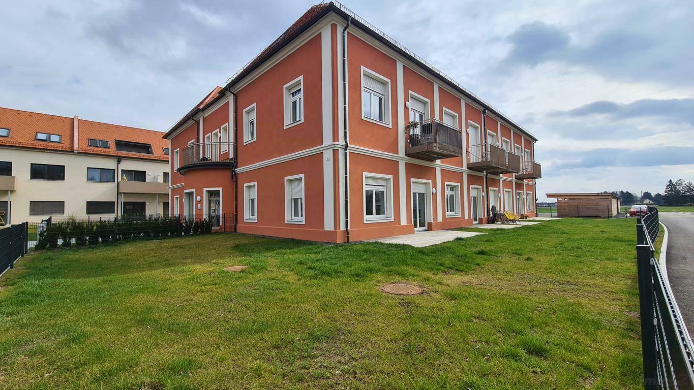 Seitenansicht des Gebäudes mit oranger Fassade, Balkonen und Grünflächen.