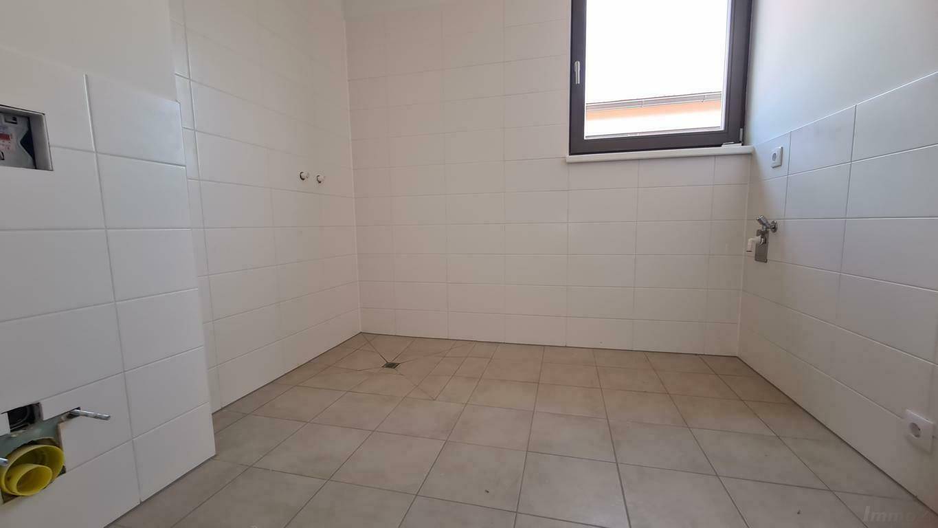 Leeres Badezimmer mit weißen Fliesen, Fenster und Anschlüssen für Sanitäranlagen.