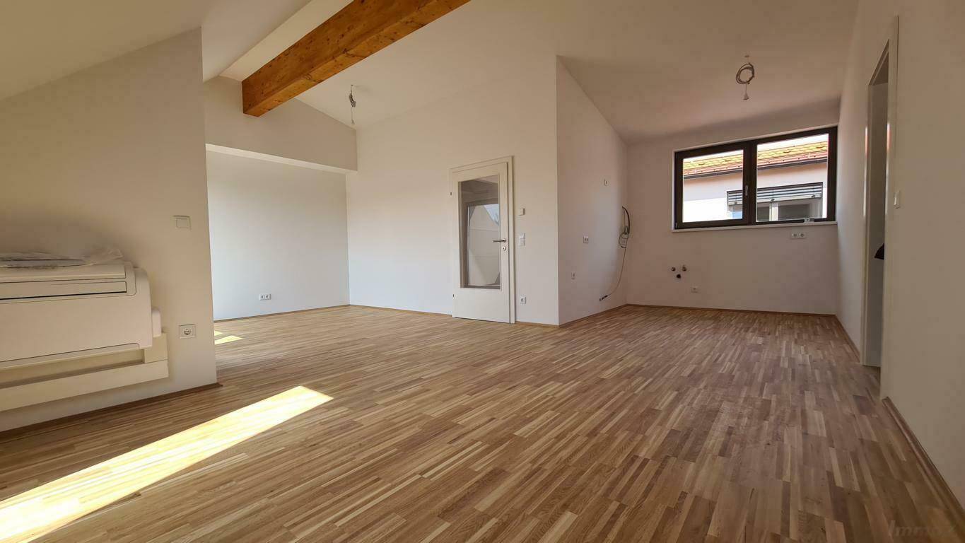 Offener, leerer Wohnbereich im Dachgeschoss mit Holzboden und Vorbereitung für eine Küche.