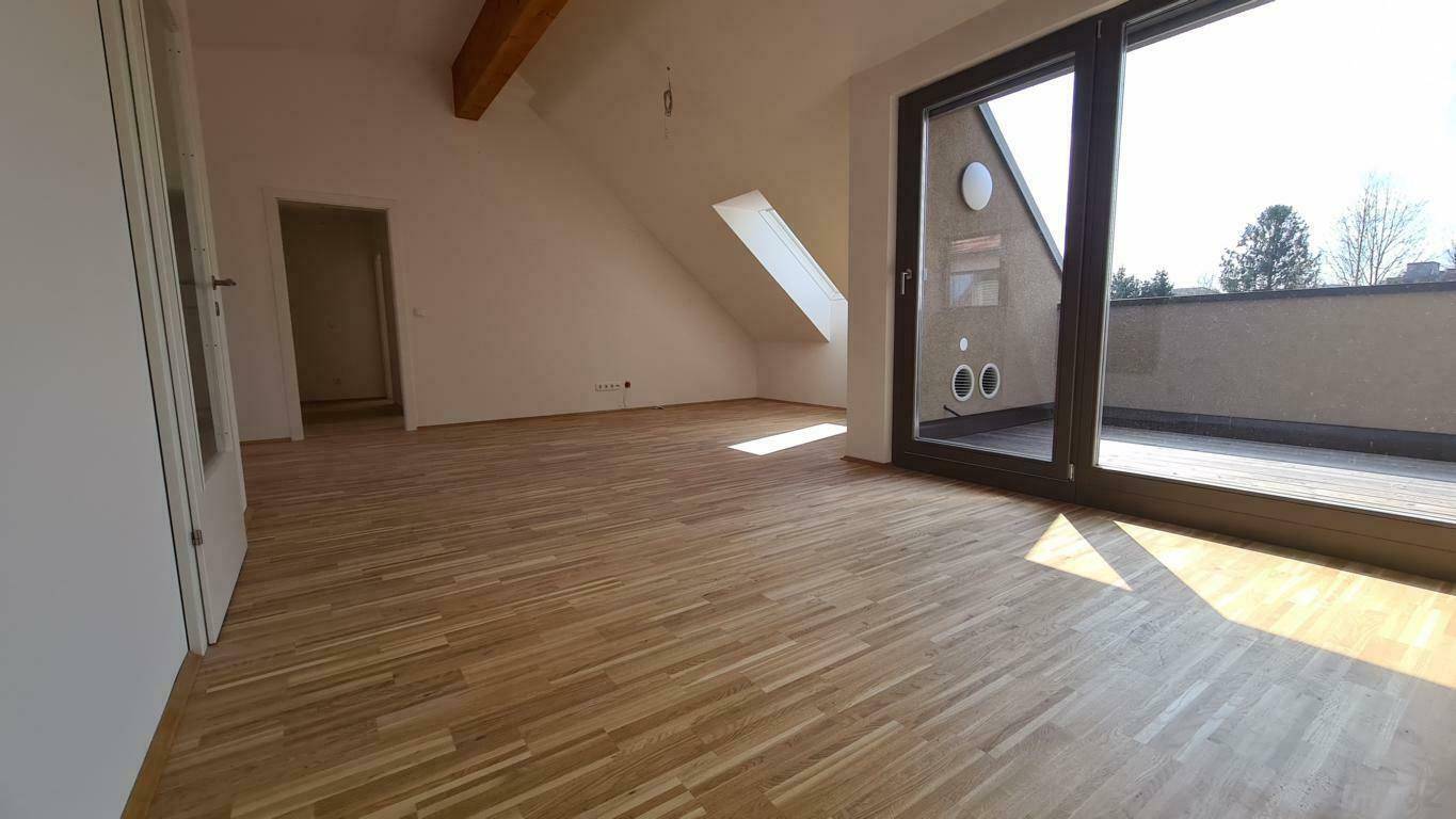Geräumiger, leerer Wohnbereich im Dachgeschoss mit Holzboden und Zugang zur Terrasse.