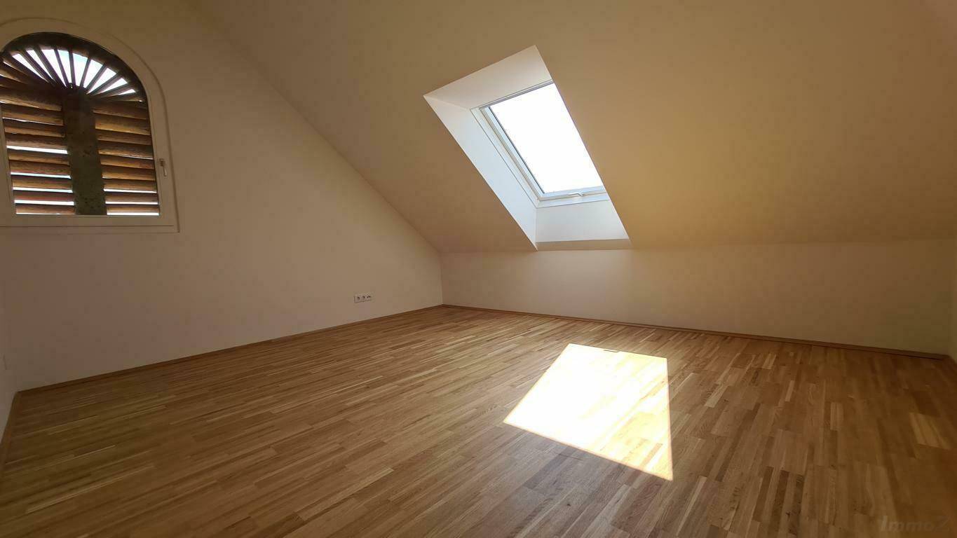 Helles, leeres Schlafzimmer im Dachgeschoss mit Holzboden und Dachfenster.