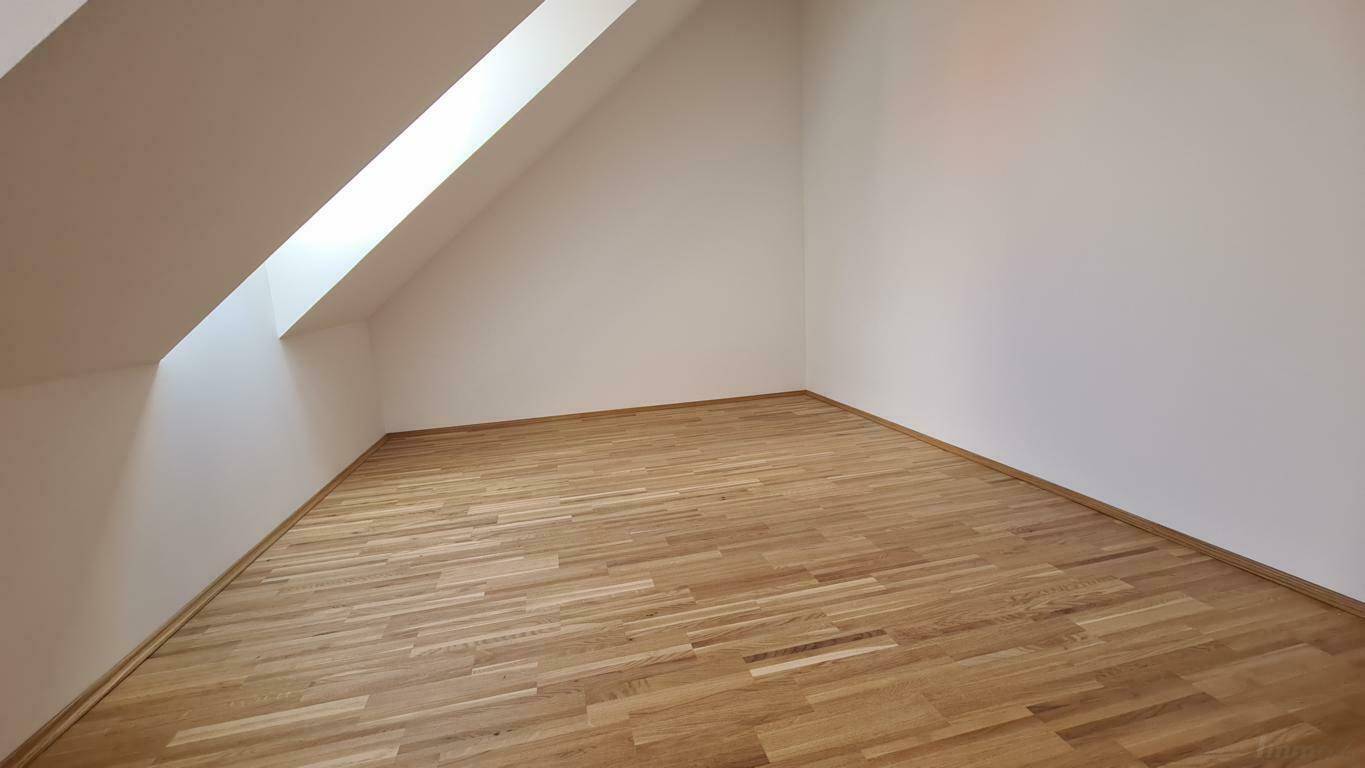 Leeres Zimmer im Dachgeschoss mit Holzboden und schrägem Dachfenster.