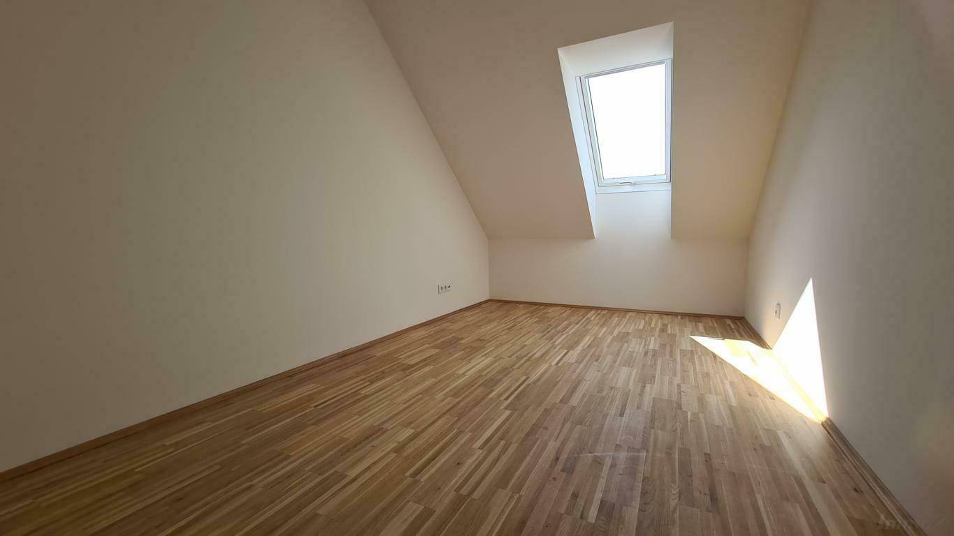 Leeres Schlafzimmer im Dachgeschoss mit Holzboden und Dachfenster, gut belichtet.
