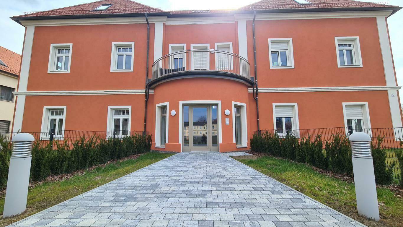 Attraktive Fassade eines modernen Wohngebäudes mit Balkon, Rollläden und gepflastertem Zugang.