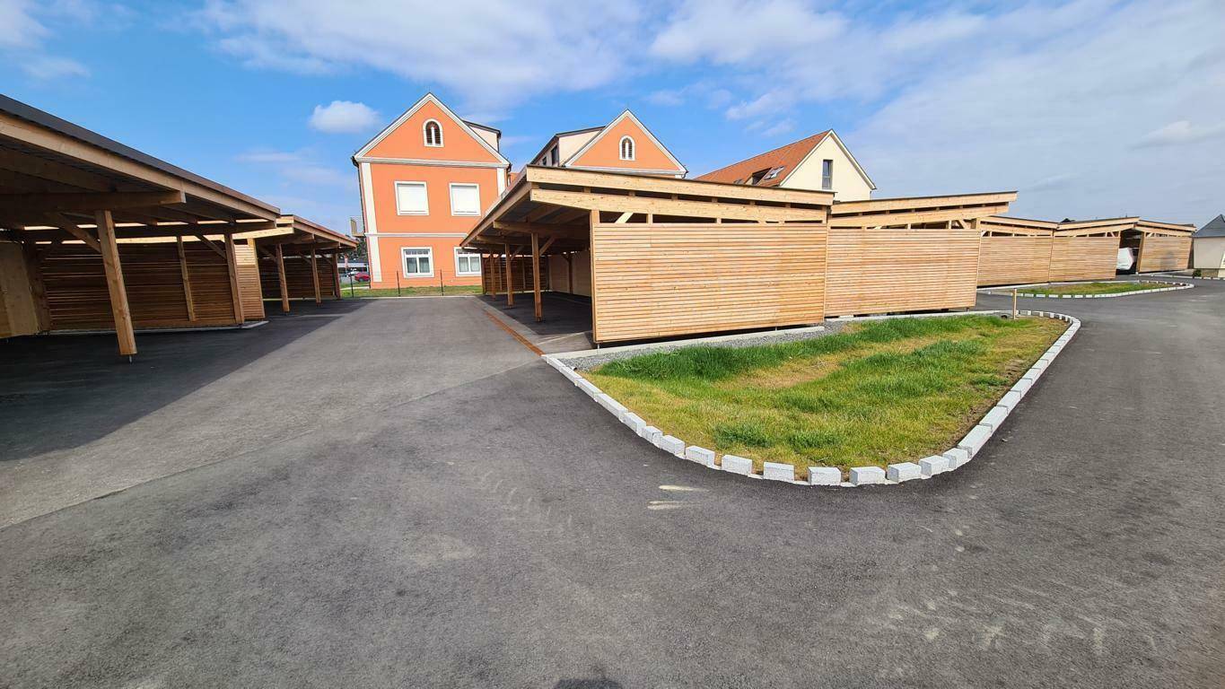 Reihe von Holz-Carports neben dem Wohngebäude unter blauem Himmel für Fahrzeuge.