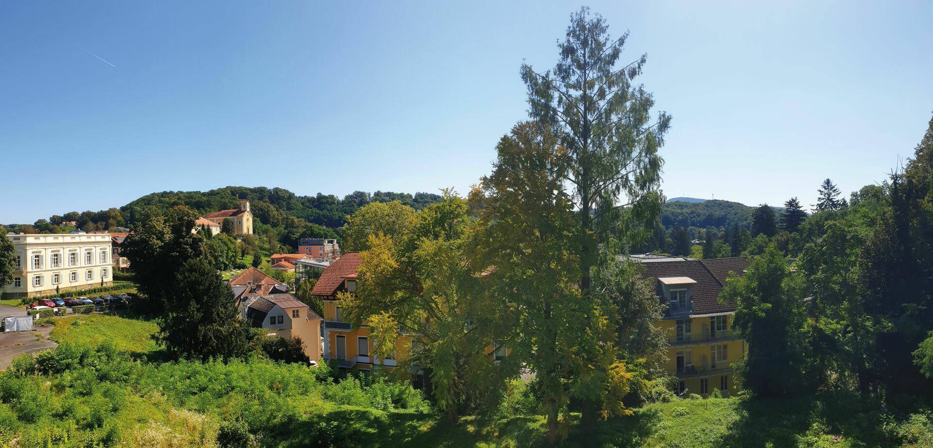 Panoramablick über eine grüne Hügellandschaft mit Häusern und einem historischen Gebäude.