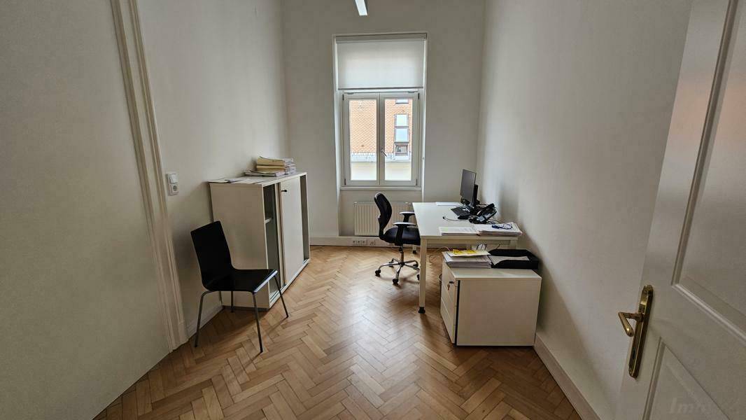 Helles Büro mit Schreibtisch, Bürostuhl und Fischgrätparkettboden.