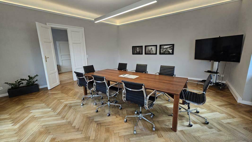 Moderner Konferenzraum mit großem Holztisch, Stühlen und einem Wandfernseher.