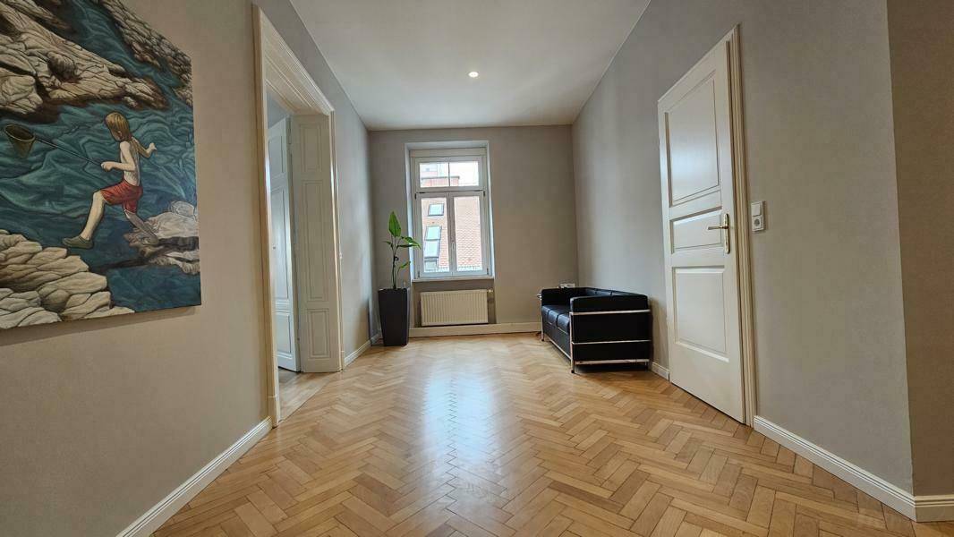 Geräumiger Flur mit Fischgrätparkett, einem Fenster und einer schwarzen Sitzbank.
