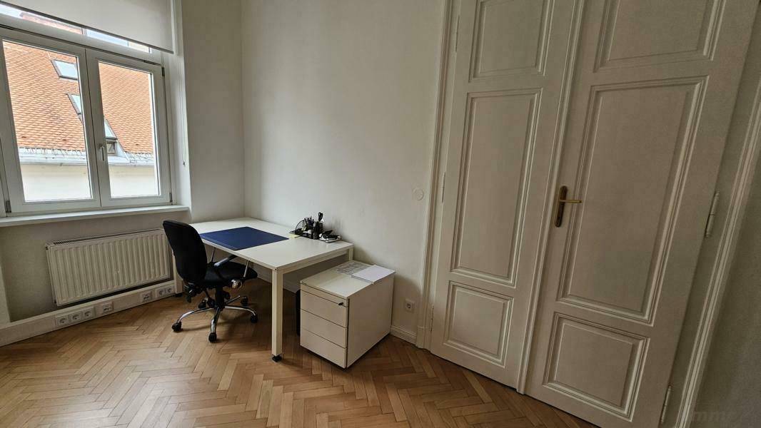 Kleiner Büroraum mit Schreibtisch, Bürostuhl und Fischgrätparkettboden.