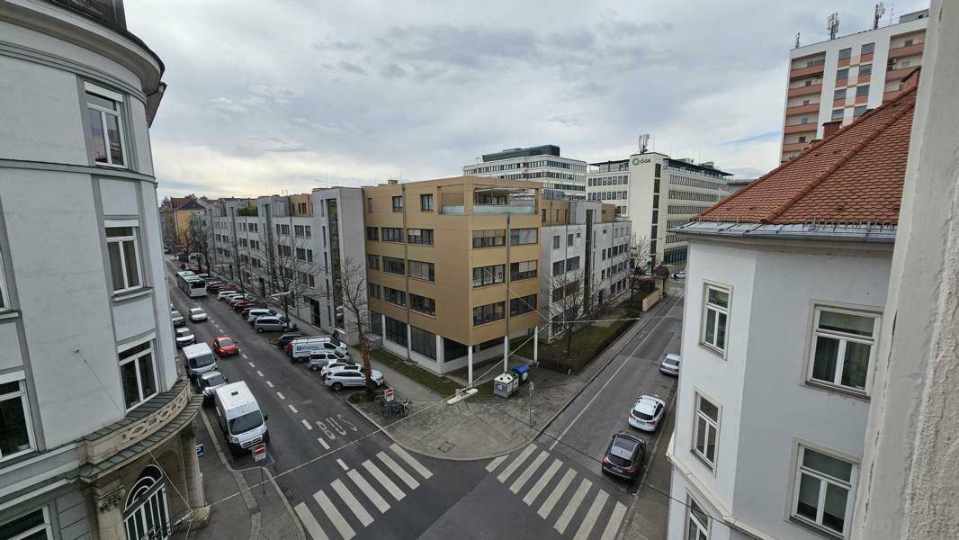 Blick auf eine belebte Stadtstraße mit Gebäuden und parkenden Autos.