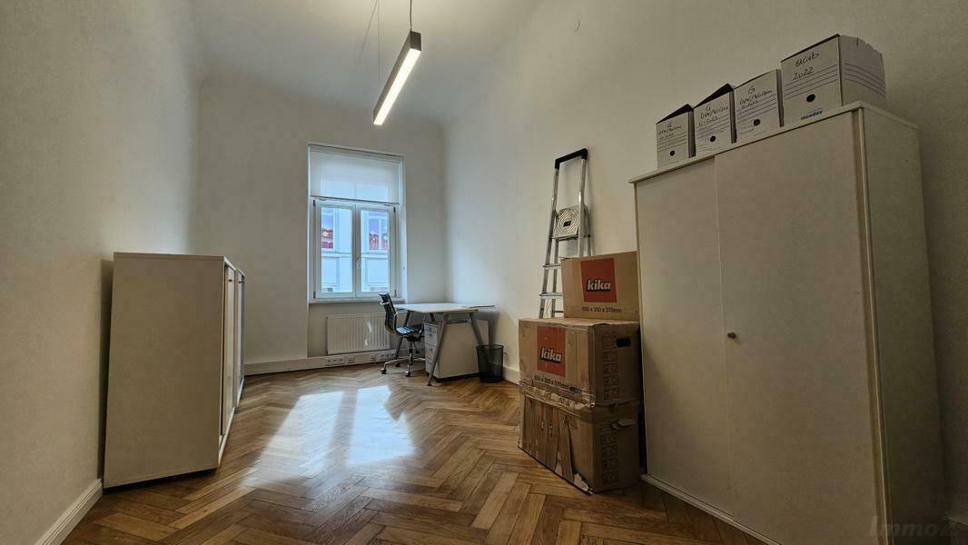 Einfacher Büroraum mit Schreibtisch, Schränken und Fischgrätparkettboden.