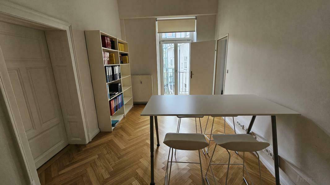 Büroraum mit Stehtisch, Hockern, Bücherregal und Zugang zu einem kleinen Balkon.