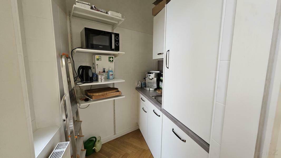 Kleine Küchenzeile mit Mikrowelle, Kaffeemaschine und weißen Schränken.
