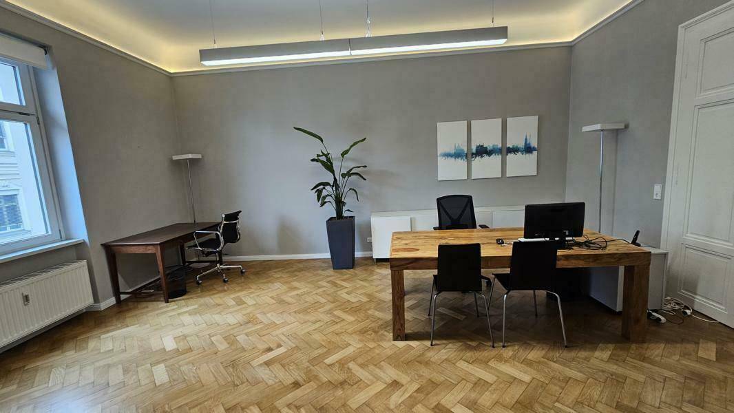 Großes Büro mit zwei Arbeitsbereichen, Fischgrätparkett und hohen Decken.