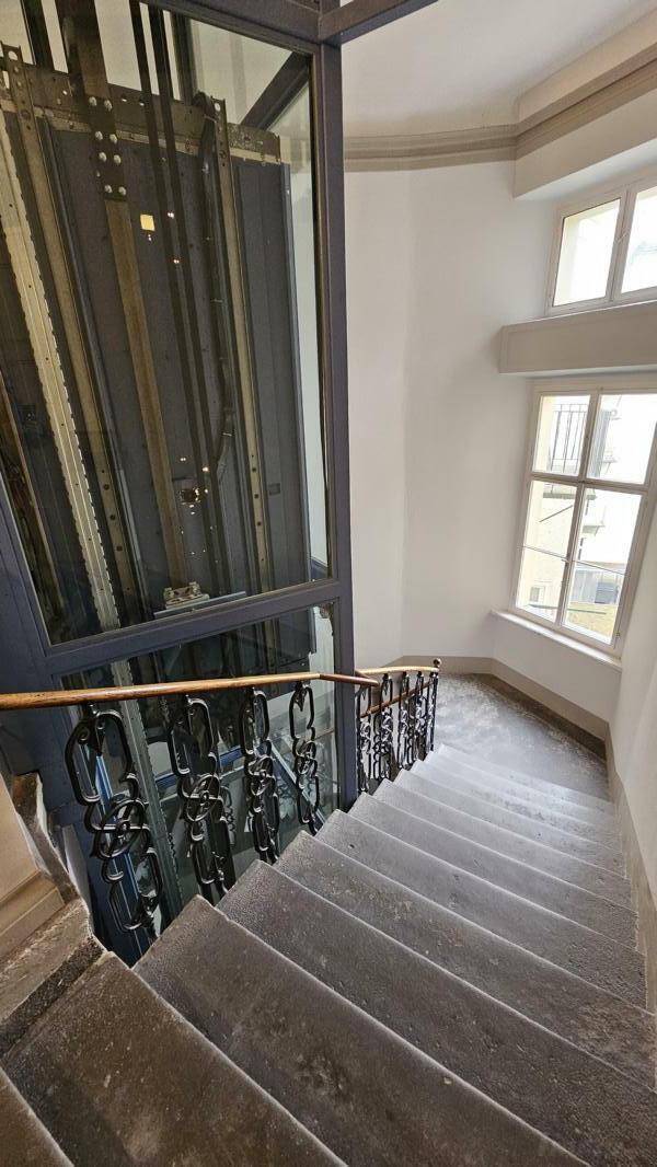 Treppenhaus mit Steinstufen und einem modernen Glasaufzug.