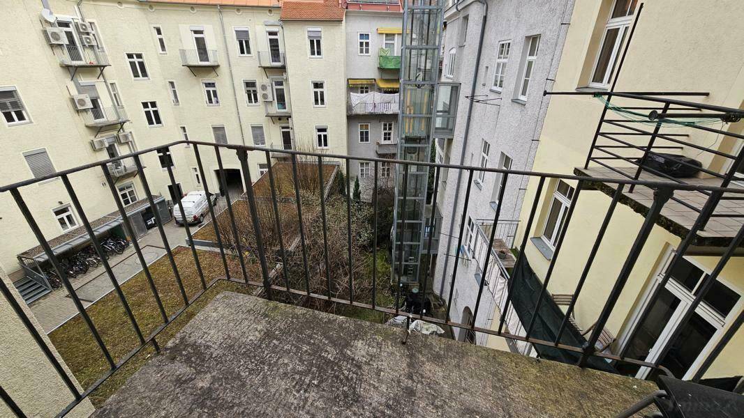 Kleiner Balkon mit Metallgeländer und Blick auf den Innenhof des Gebäudes.