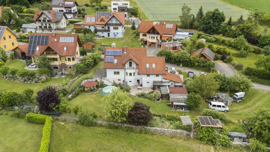 Luftaufnahme einer Wohnsiedlung mit mehreren Häusern, umgeben von viel Grün und Feldern.