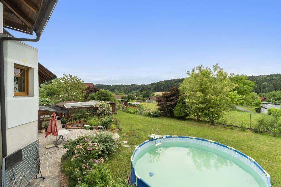 Panoramablick von einer erhöhten Terrasse auf den Garten mit Pool und die grüne Umgebung.
