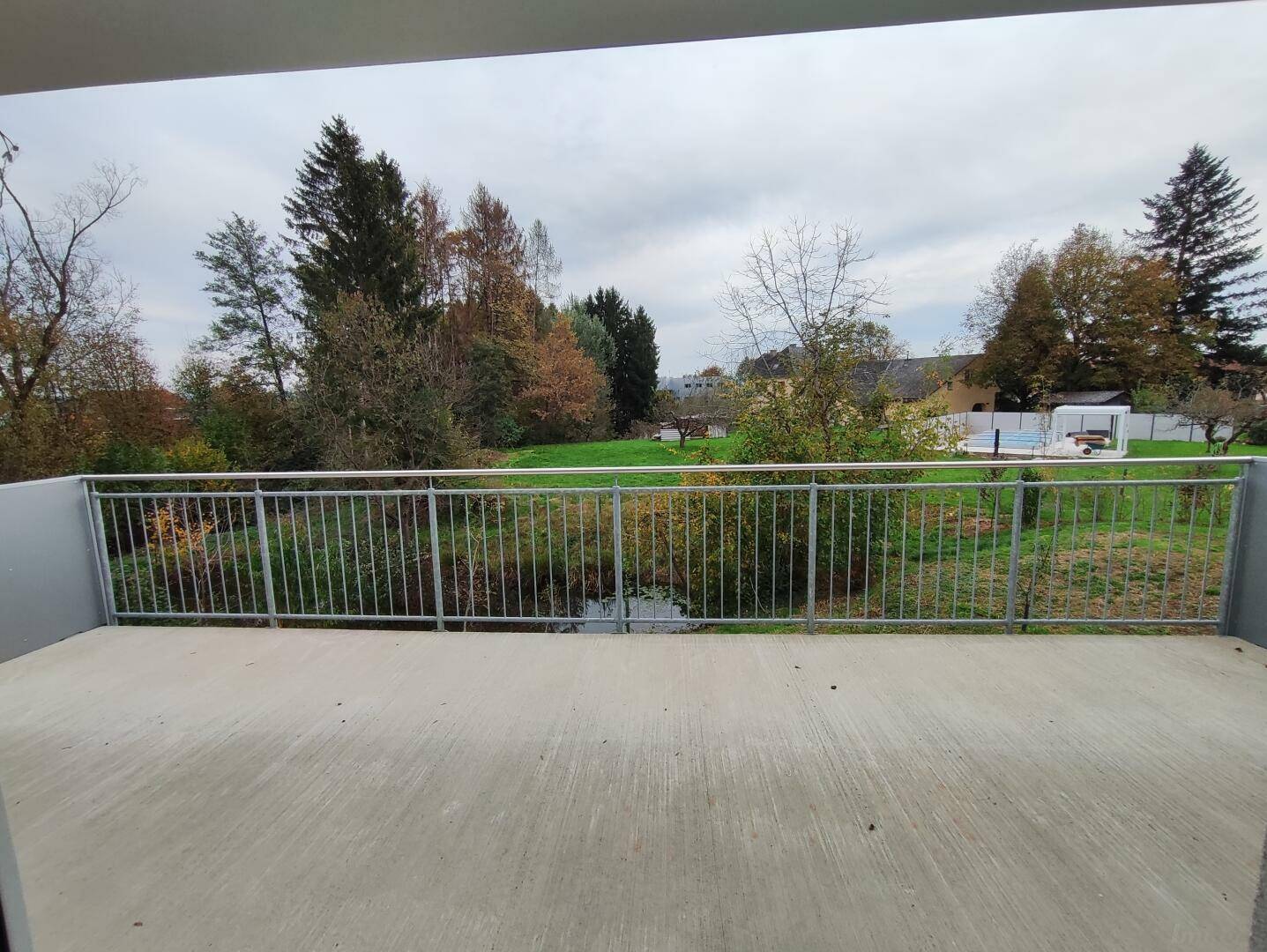 Balkon mit weitem Blick über eine grüne Landschaft, Bäume und einen entfernten Poolbereich.