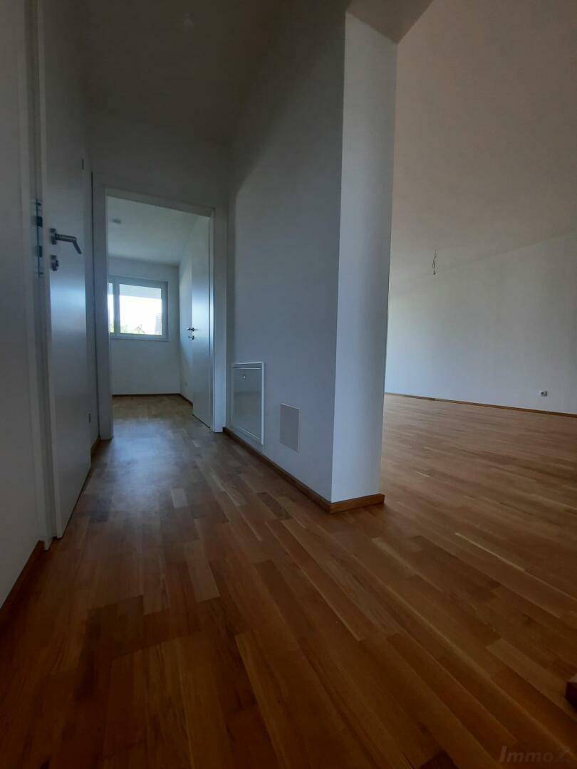 Heller Flur mit Echtholzparkettboden und weißen Wänden, der zu weiteren Zimmern führt.