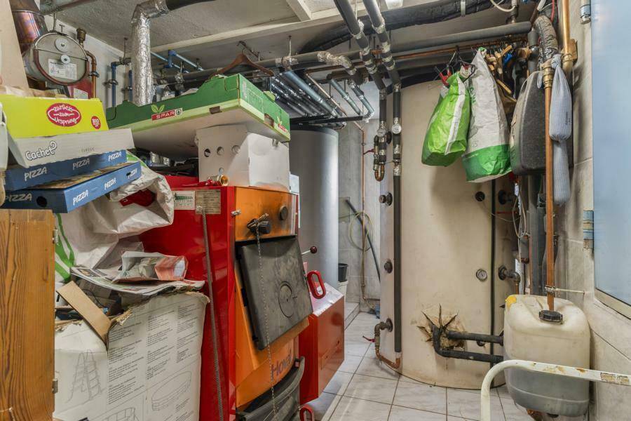 Heizungsraum im Keller mit Heizkessel, Warmwasserspeicher und sichtbaren Rohren.