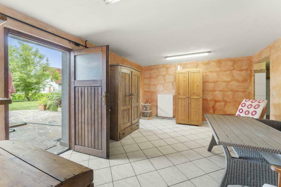 Heller Kellerraum mit Fliesenboden, Holzmöbeln und direktem Ausgang ins Freie.