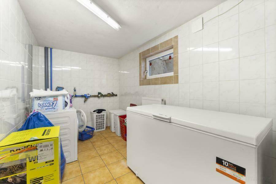Waschküche im Keller mit Waschmaschine, Gefriertruhe und gefliestem Boden.