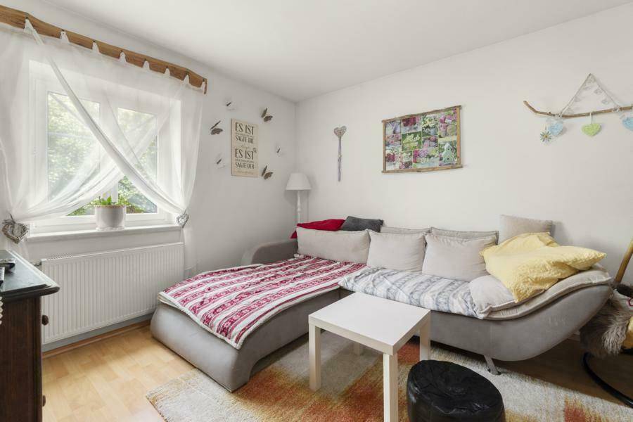 Helles Wohnzimmer mit bequemer Couch, Fenster und Blick ins Grüne.