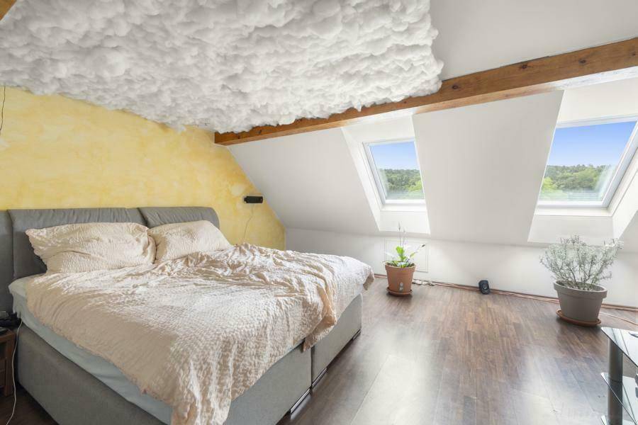 Helles Schlafzimmer im Dachgeschoss mit Dachschrägen, zwei Dachfenstern und dunklem Laminatboden.