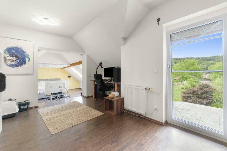 Helles Arbeitszimmer im Dachgeschoss mit Zugang zu einem Balkon und Blick ins Grüne.