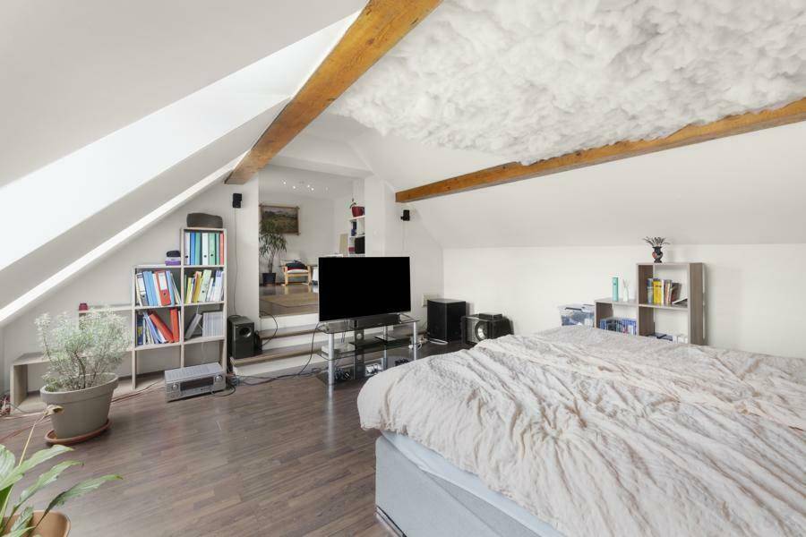 Gemütliches Schlafzimmer im Dachgeschoss mit Holzbalken, Dachschrägen und dunklem Laminatboden.