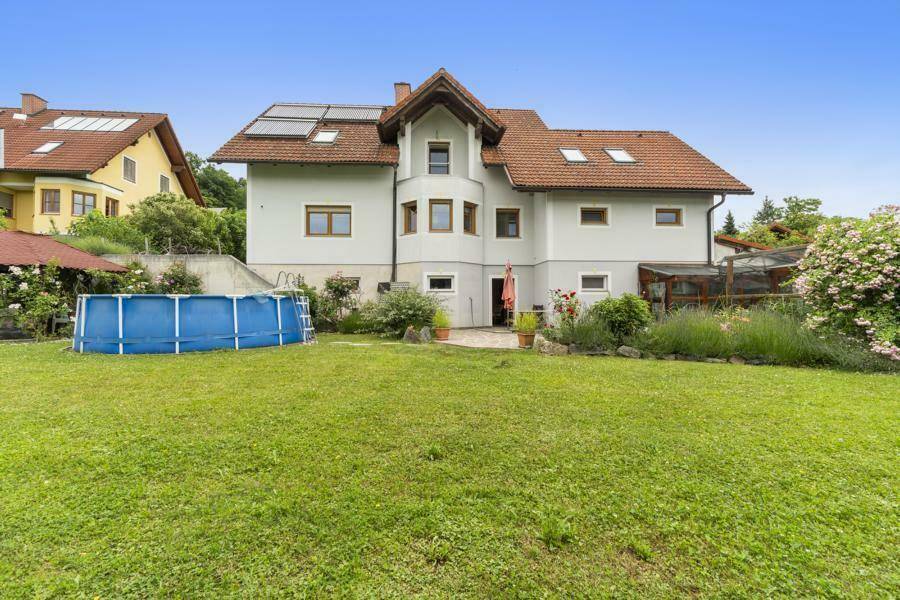Rückansicht des Hauses mit großem Garten, Rasenfläche und einem Aufstellpool unter blauem Himmel.