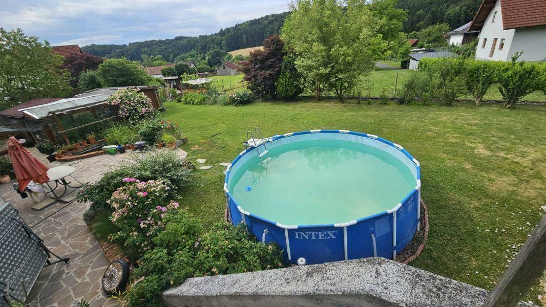 Blick von oben auf den Garten mit Aufstellpool, gepflasterter Terrasse und grüner Landschaft.
