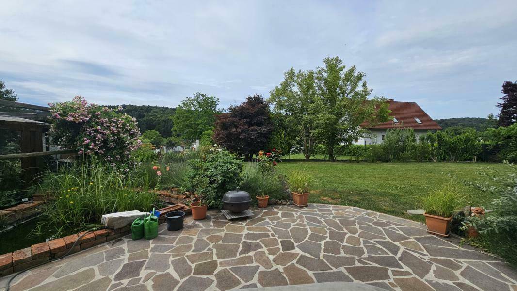 Große, gepflasterte Terrasse mit Grillbereich und Blick auf den weitläufigen Garten.