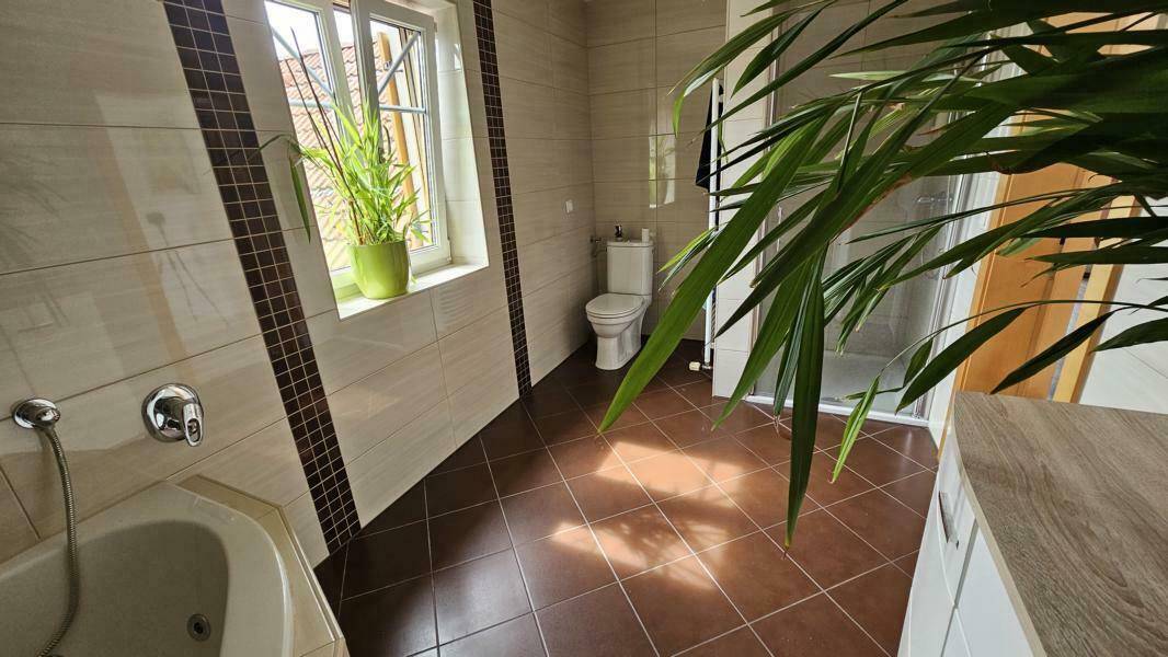 Modern gefliestes Badezimmer mit Badewanne, Toilette und separater Duschkabine.