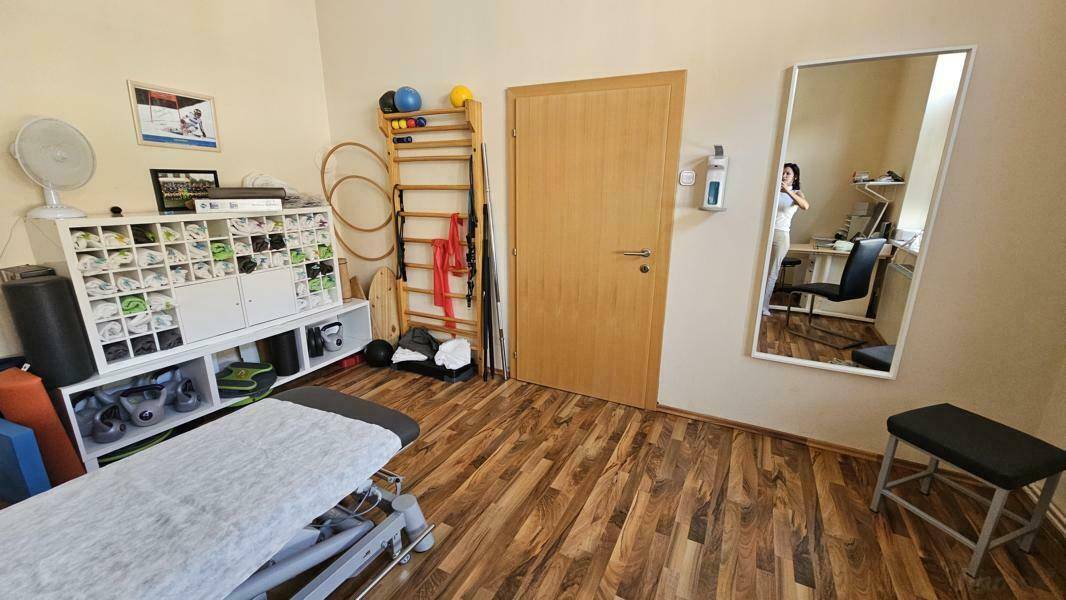 Funktional eingerichtetes Zimmer, möglicherweise als Büro oder Therapieraum genutzt, mit Holzboden.