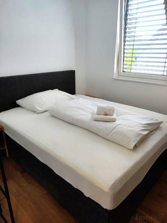 Helles Schlafzimmer mit Einzelbett, Holzboden und Fenster mit Jalousien.