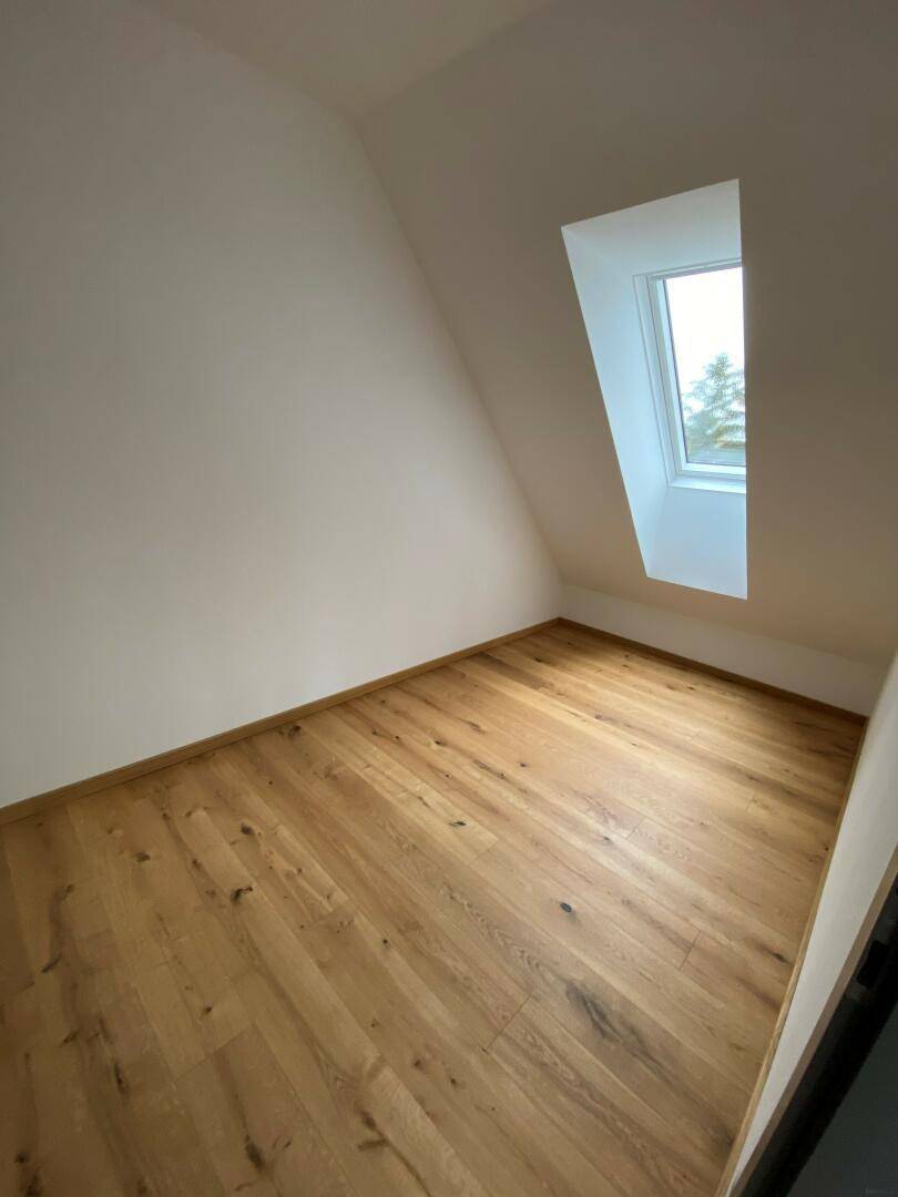 Helles Dachzimmer mit Holzboden und Dachfenster, ideal als Schlaf- oder Arbeitszimmer.