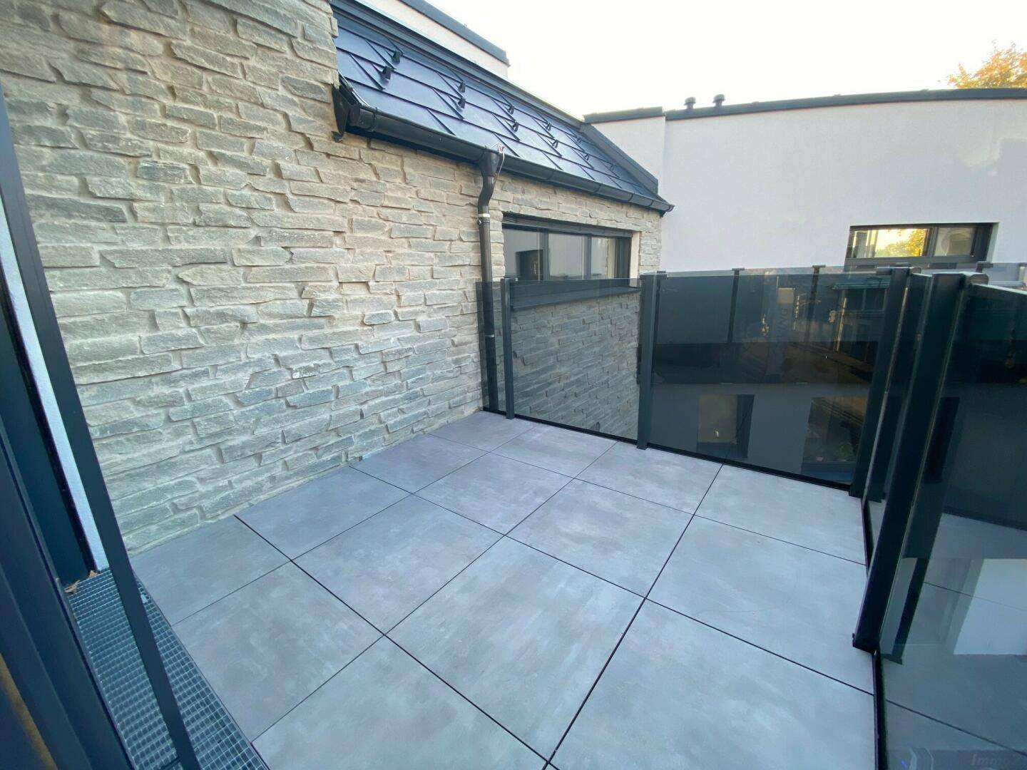 Abgeschirmter Terrassenbereich mit Steinwand und modernen Bodenfliesen.
