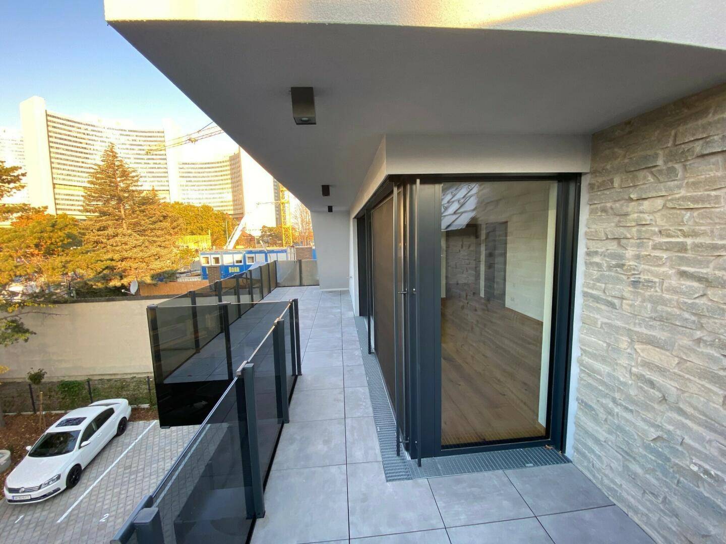Lange Terrasse mit modernen Fliesen und Glasgeländer, angrenzend an den Wohnbereich.