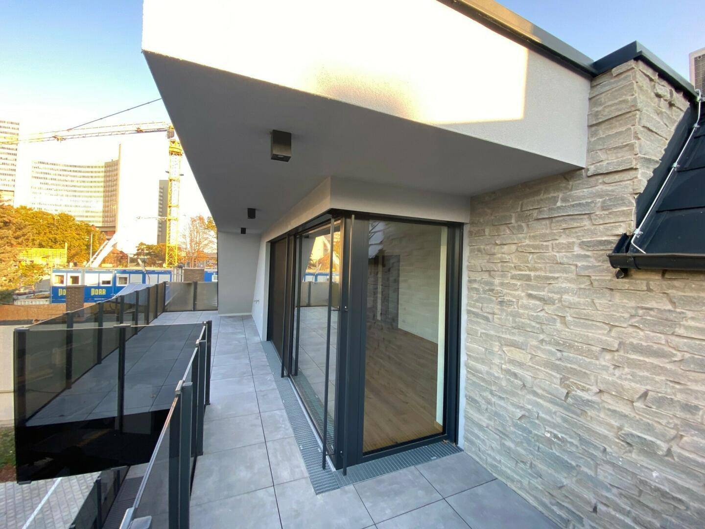 Moderne Terrasse mit Steinverkleidung an der Fassade und großen Schiebetüren.