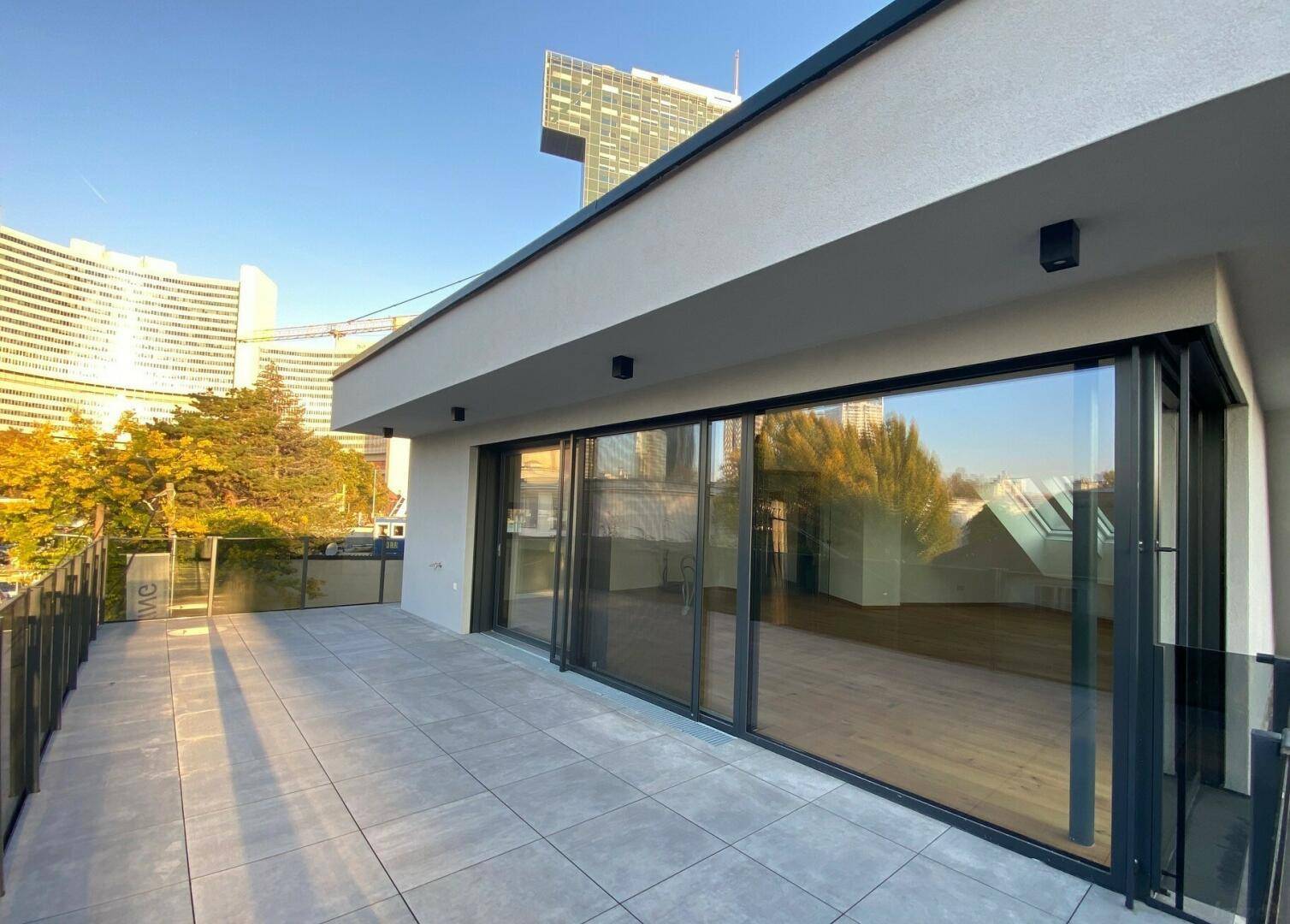 Geräumige Terrasse mit modernen Fliesen und großen Glasfronten, die in den Wohnbereich führen.