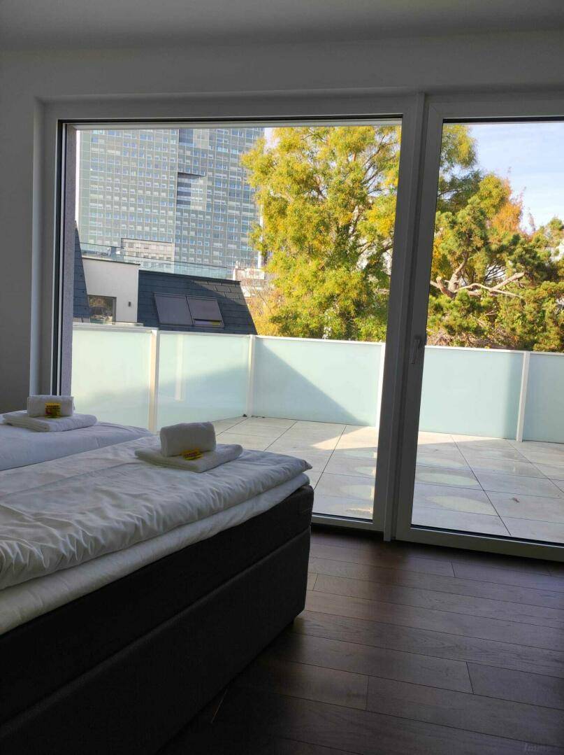 Schlafzimmer mit großen Fenstern und direktem Zugang zu einer sonnigen Terrasse.