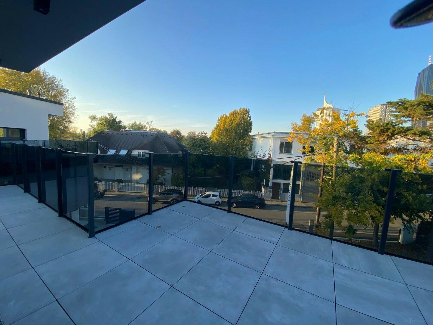Weitläufige Terrasse mit Glasgeländer und Blick auf die ruhige Wohngegend und Bäume.